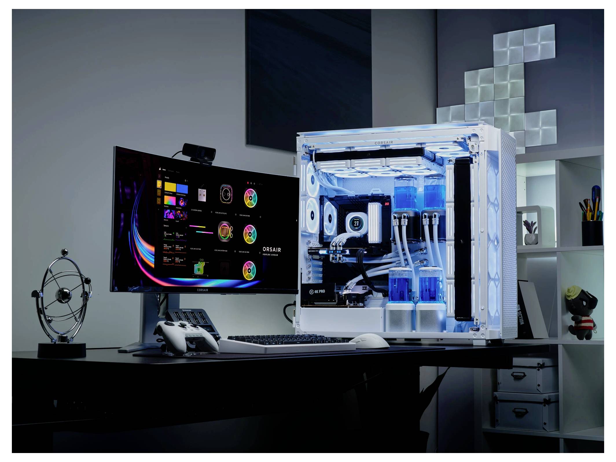 Ein Desktop-Computer mit einem großen Monitor zeigt bunte Systemstatistiken. Daneben steht ein beleuchtetes Gehäuse mit Wasserkühlung.
