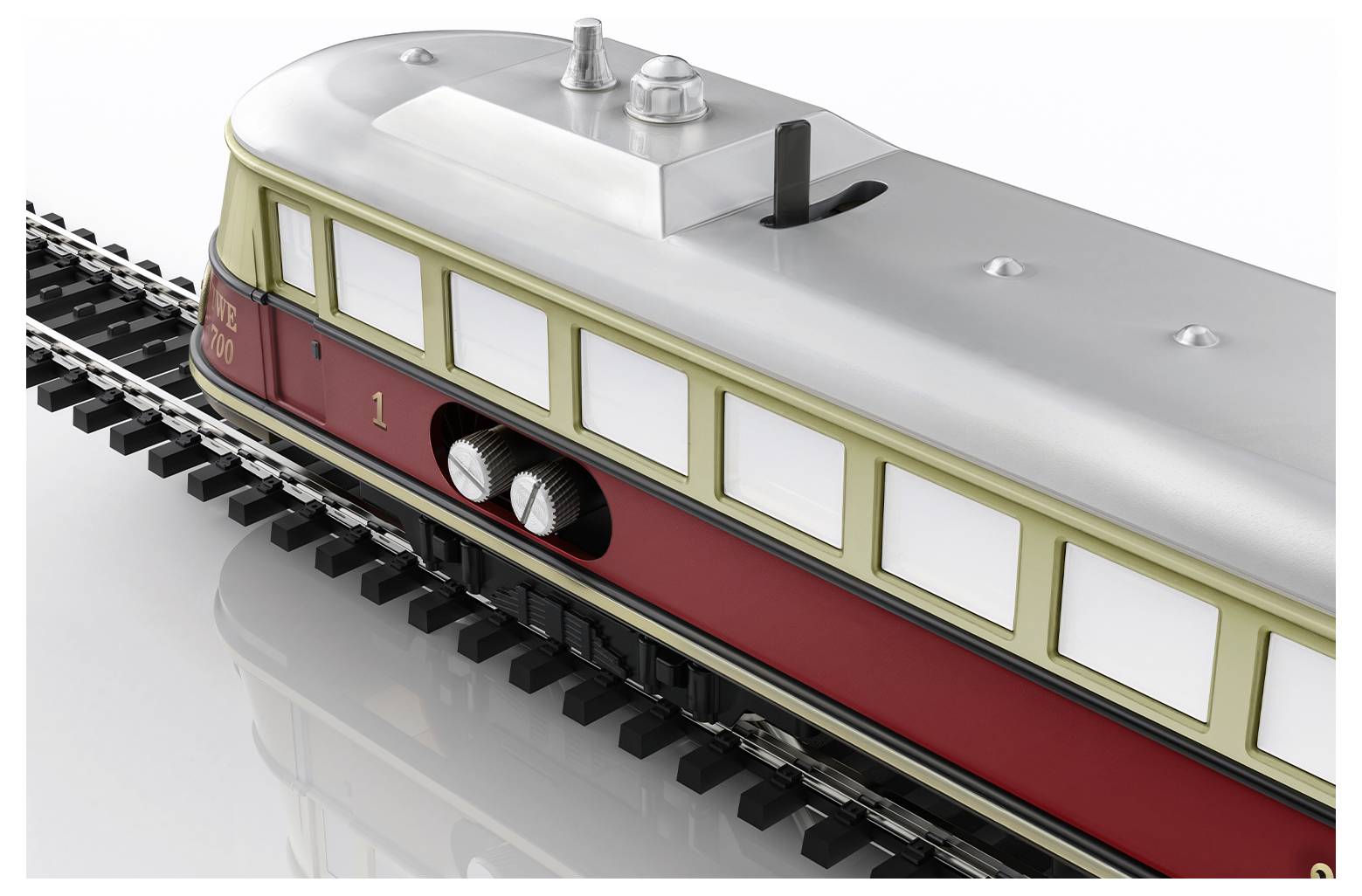 Ein Modellzug in rot-beige Farben fährt auf Gleisen. Das Fenster an der Seite zeigt den Innenraum mit sichtbaren Gepäckfächern.