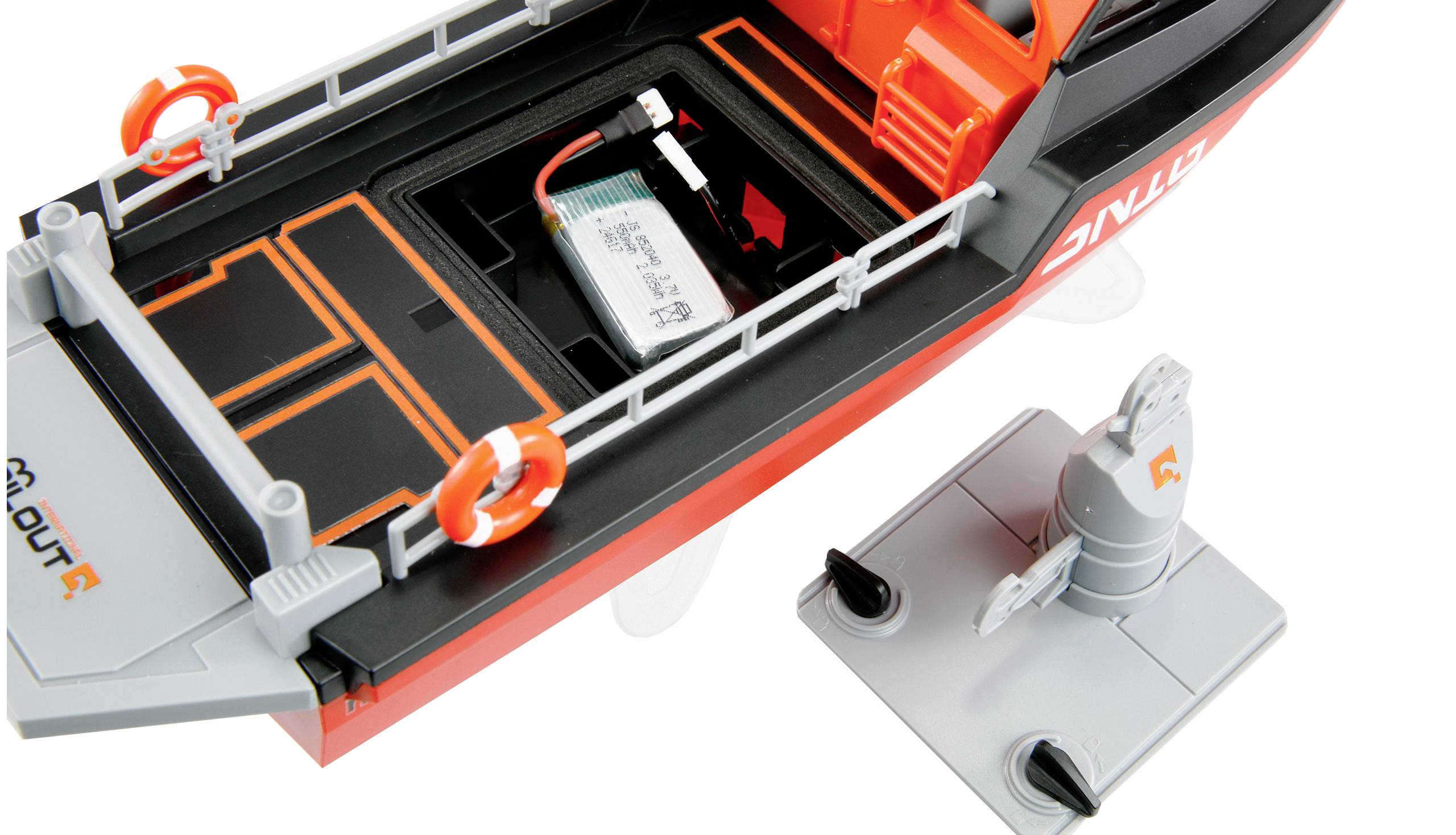 Ein Modellboot mit geöffnetem Batteriefach. Neben dem Boot liegt ein separat abgebildetes Zubehörteil.
