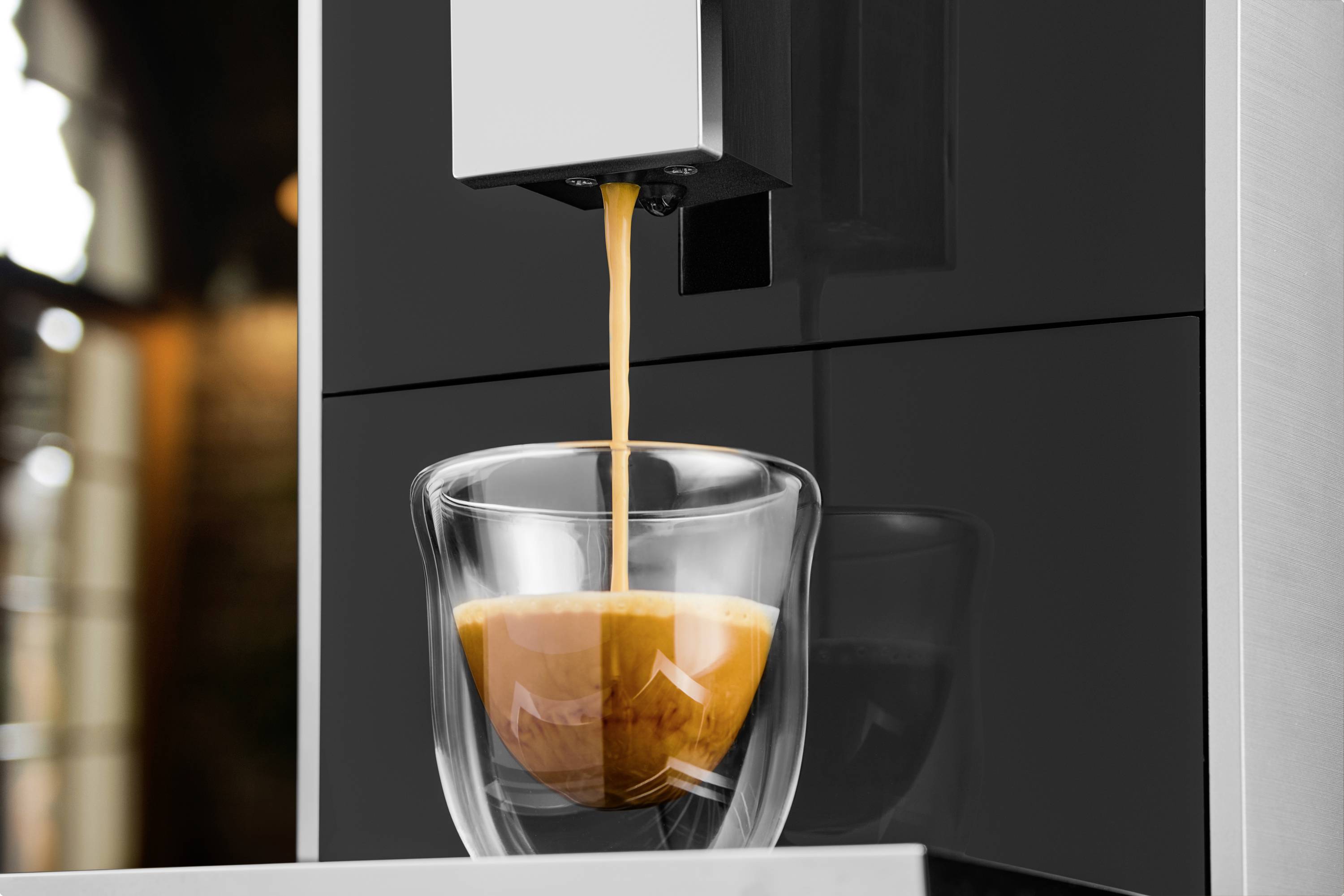 Eine Espressomaschine füllt eine Tasse mit frischem Espresso. Der dunkle Kaffee fließt in eine transparente Glastasse.