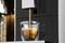 Eine Espressomaschine füllt eine Tasse mit frischem Espresso. Der dunkle Kaffee fließt in eine transparente Glastasse.