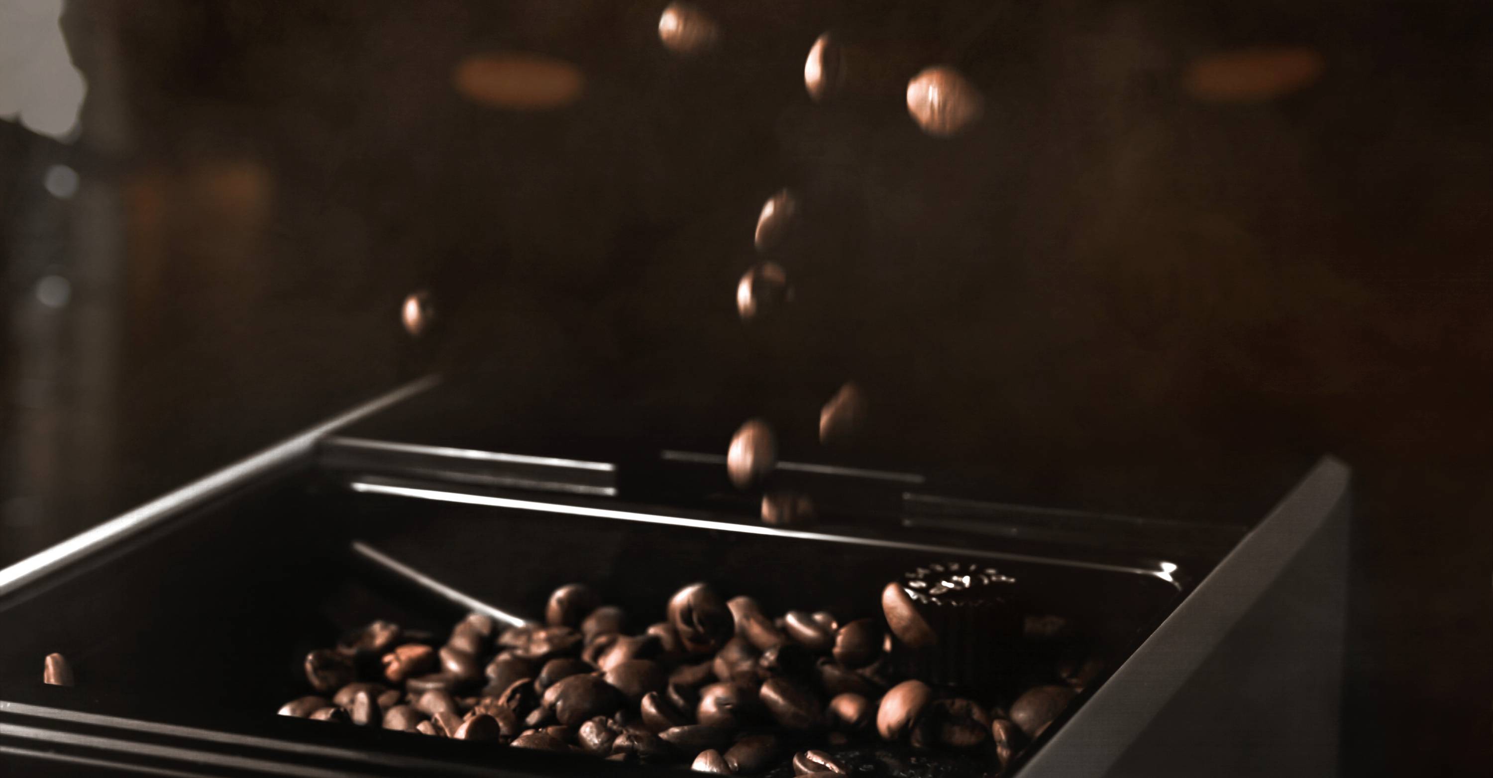 Kaffeebohnen fallen in eine Kaffeemühle, umgeben von dunklem Hintergrund, der eine warme und gemütliche Atmosphäre vermittelt.