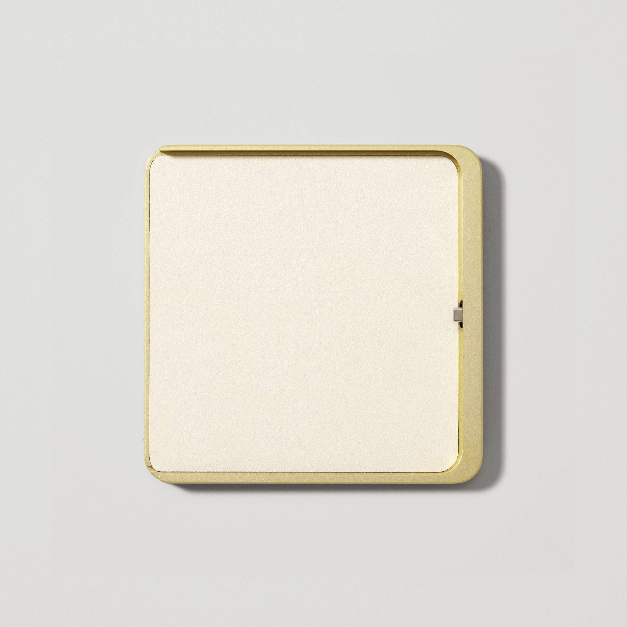 Weiße quadratische Notiztafel mit goldfarbenem Rahmen auf grauem Hintergrund.
