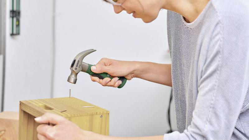 Eine Person hämmert einen Nagel in ein Holzstück.