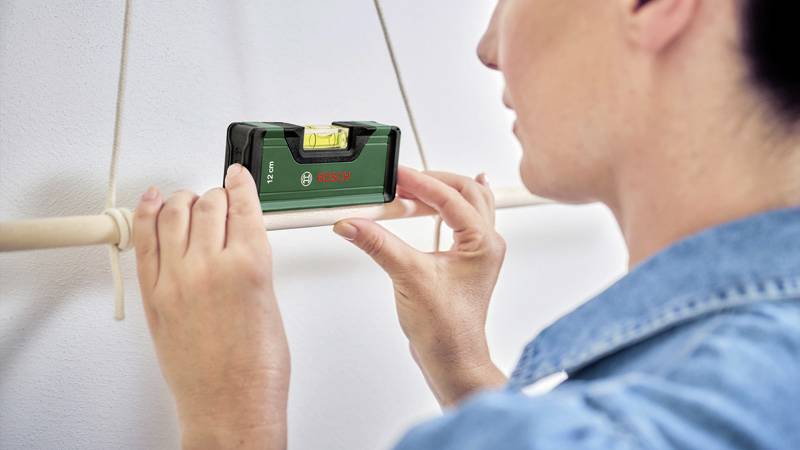 Eine Person überprüft mit einer Wasserwaage die horizontale Ausrichtung eines Stabes an der Wand.