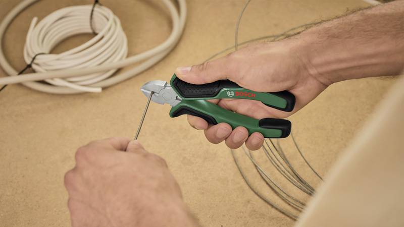 Eine Hand hält einen Drahtschneider der Marke Bosch. Im Hintergrund sind aufgerollte Kabel zu sehen.