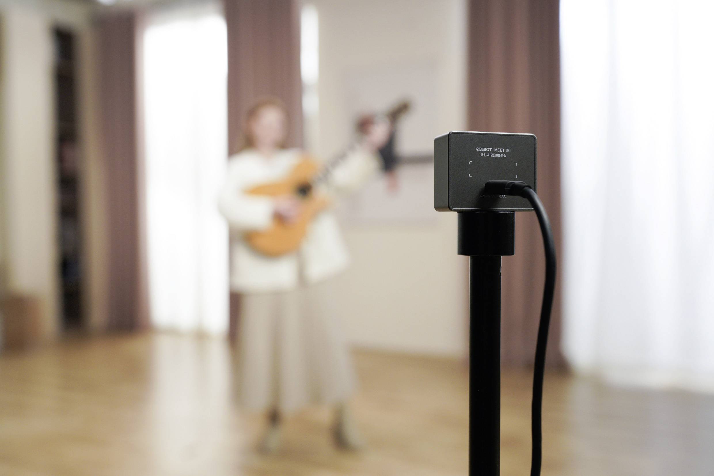 Eine Person spielt Gitarre im Hintergrund, während im Vordergrund eine Kamera auf einem Stativ fokussiert ist.