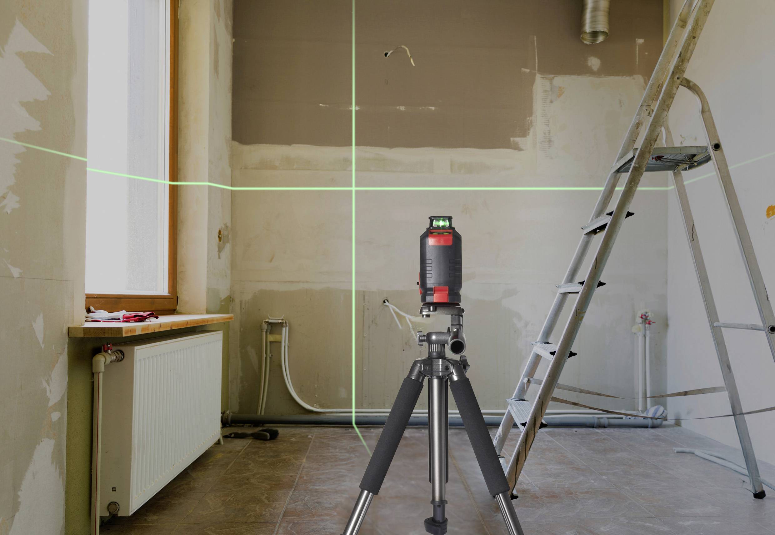 Ein Lasernivelliergerät steht im Mittelpunkt eines teilweise renovierten Raums mit Leitern und offenen Rohren an den Wänden.