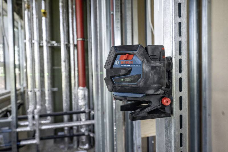 Ein Bosch-Laser-Messgerät auf einer Halterung an einer Metallwand in einer Baustelle zur genauen Nivellierung oder Ausrichtung.