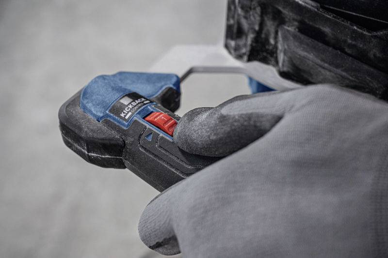 Eine Hand in einem grauen Handschuh hält eine Zange mit blauem und schwarzem Griff, die eine rote Taste hat.