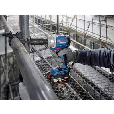 Eine Person verwendet einen blauen Akkuschlagschrauber, um eine Schraube an einem metallischen Gerüst zu befestigen. Im Hintergrund ist das Gerüst einer Baustelle zu sehen.