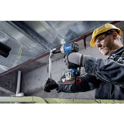 Ein Bauarbeiter mit Helm und Handschuhen befestigt ein Metallblech an der Decke mit einem blauen Elektrowerkzeug in einer Industrieumgebung.