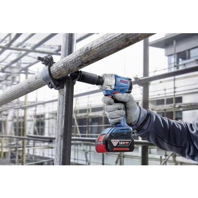 Eine Person arbeitet mit einem blauen, akkubetriebenen Schraubendreher an einem Gerüst im Freien. Im Hintergrund ist ein Gebäude sichtbar.