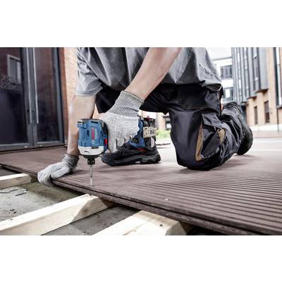 Eine Person kniet und verwendet einen Elektrobohrer, um Holzbretter auf einem Terrassenboden zu befestigen.