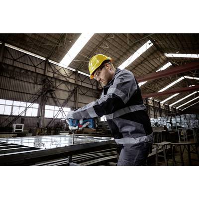 Ein Arbeiter in Schutzkleidung und Helm bohrt Metall in einer großen Fabrikhalle.