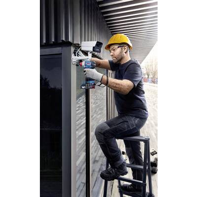 Ein Arbeiter mit Schutzhelm und Handschuhen installiert eine Überwachungskamera an der Außenwand eines modernen Gebäudes.