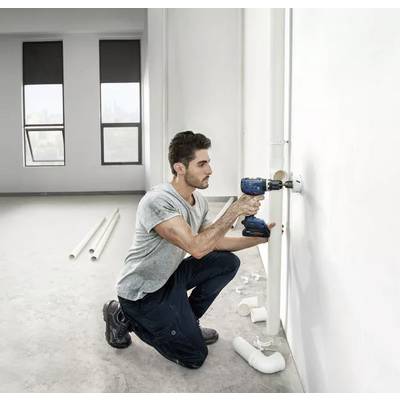 Ein Mann kniet auf dem Boden und hält eine Bohrmaschine an die weiße Wand eines leeren Raumes. Intelligenter Einsatz von BiTurbo Technology.
