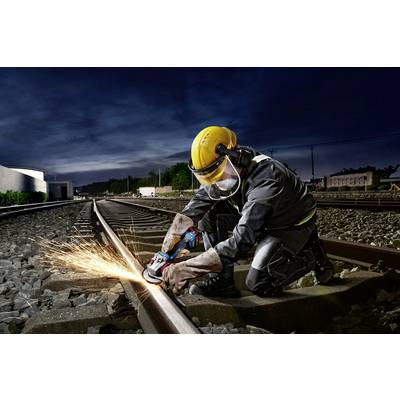Eine Person in Schutzkleidung schneidet mit einem Winkelschleifer Metall auf Bahngleisen. Funken fliegen unter dunklem Himmel.