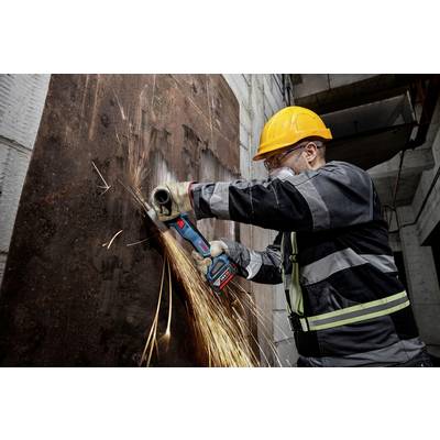 Ein Arbeiter mit Schutzhelm und Brille schneidet mit einem Winkelschleifer Metall, Funken fliegen in einem industriellen Umfeld.