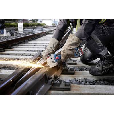 Ein Arbeiter trägt Schutzhandschuhe und bearbeitet mit einem Winkelschleifer ein Gleis, Funken sprühen beim Schleifen der Schiene.