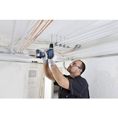 Ein Handwerker befestigt mit einem Akkuschrauber Rohre an der Decke eines Raumes, während er Schutzbrille und Arbeitshandschuhe trägt.