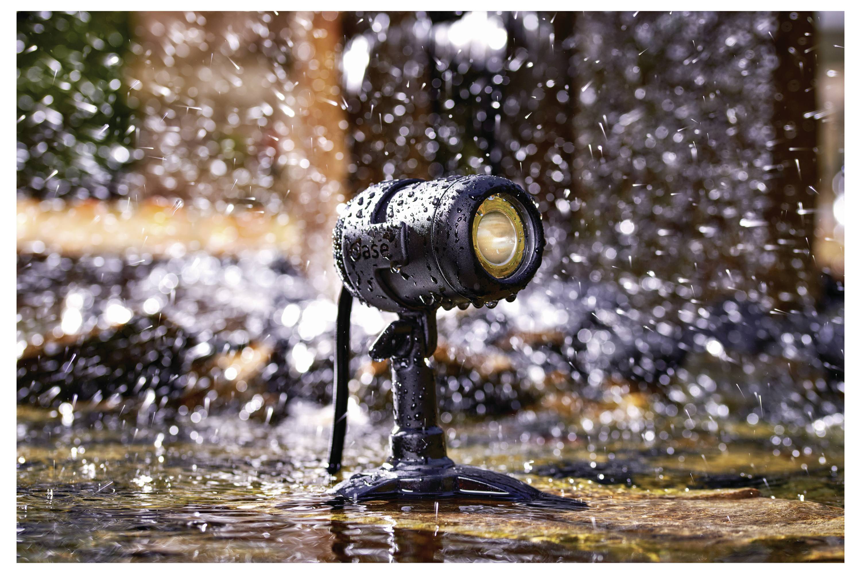 Eine kleine, wasserdichte Strahlerlampe, die mit Wassertropfen bedeckt ist, ist auf einer nassen Oberfläche befestigt, während im Hintergrund Wasser spritzt.