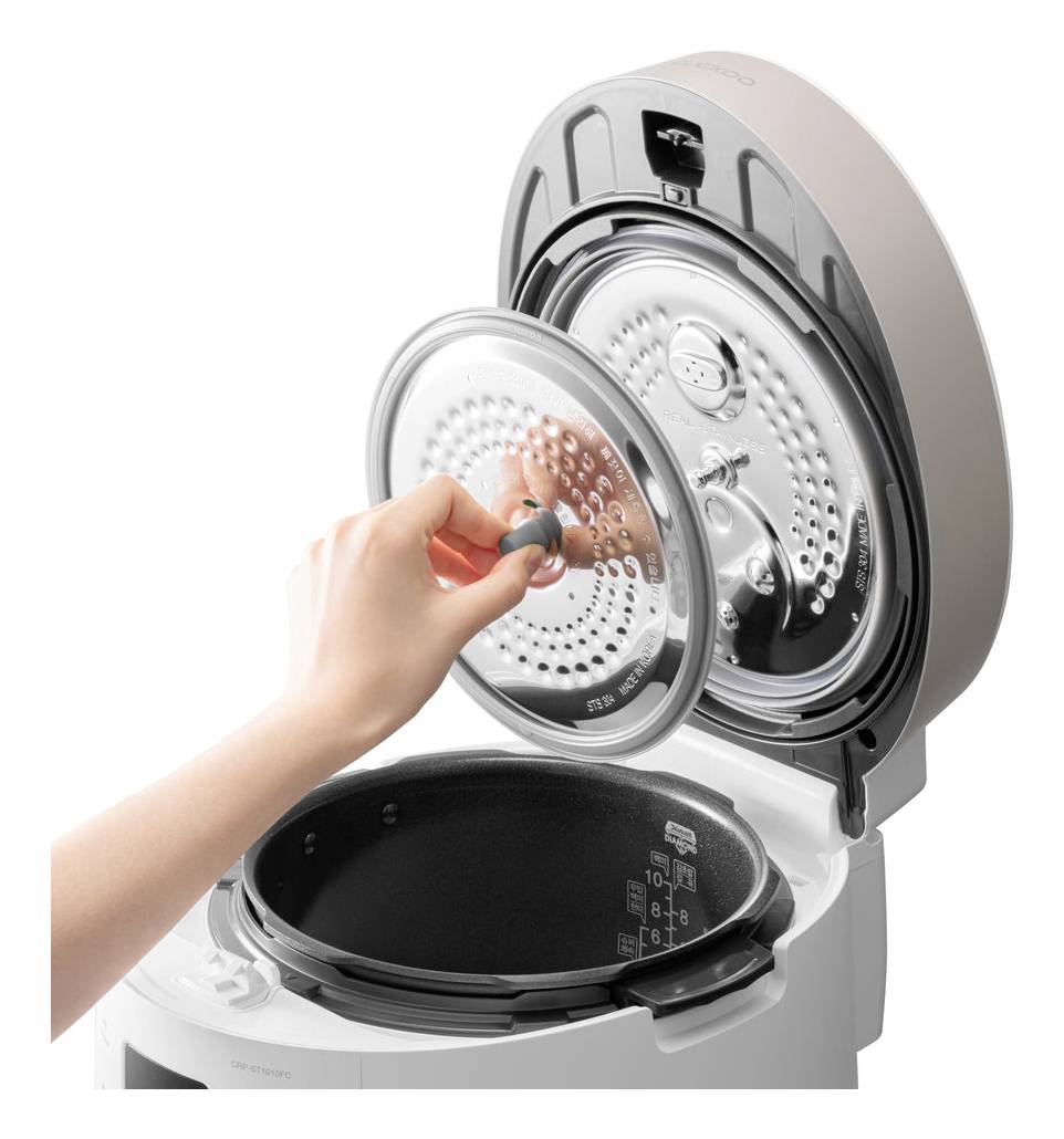 Eine Hand öffnet den Deckel eines modernen Reiskochers, zeigt das Innere mit Messskala und Dampfventil.