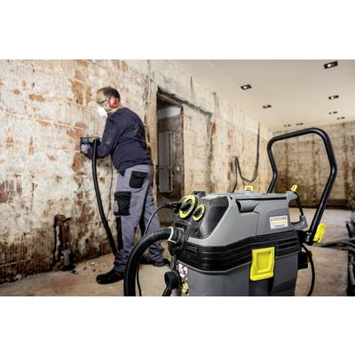 Ein Handwerker entfernt alten Putz von einer Wand mit einem Bohrhammer. Im Vordergrund steht ein Industriesauger, der Staub aufsaugt.