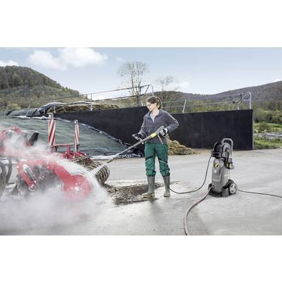Eine Person reinigt landwirtschaftliche Maschinen mit einem Hochdruckreiniger auf einem Bauernhof im Freien.