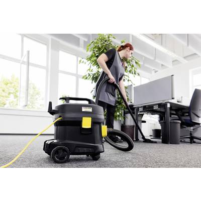 Eine Frau saugt ein Büro mit einem Industriestaubsauger. Im Hintergrund stehen Schreibtische und ein großer grüner Pflanztopf.