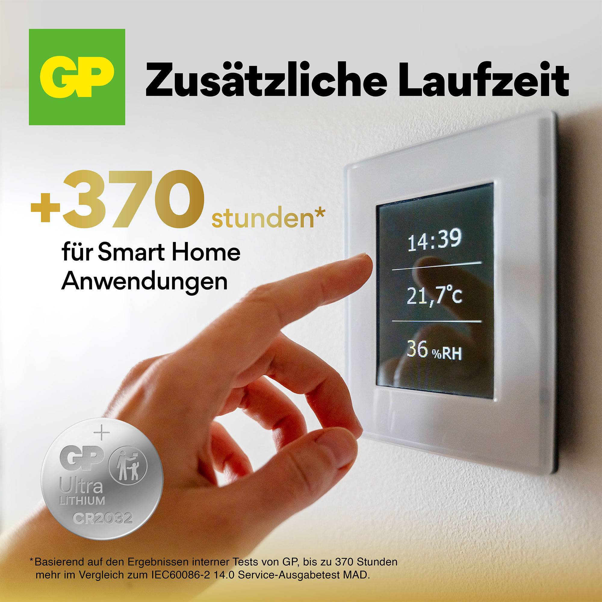 Finger zeigt auf ein smartes Home-Thermostat an der Wand, Anzeige: 21,7°C, 36% Luftfeuchtigkeit. Werbung für GP-Batterien, 'Zusätzliche Laufzeit +370 stunden'.