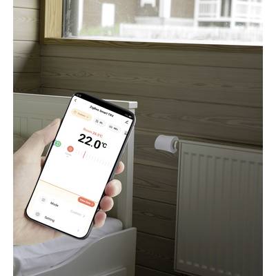 Ein Smartphone in der Hand zeigt eine App zur Steuerung der Raumtemperatur an, die 22,0°C und den Modus 'Custom' anzeigt. Im Hintergrund läuft eine Heizung.