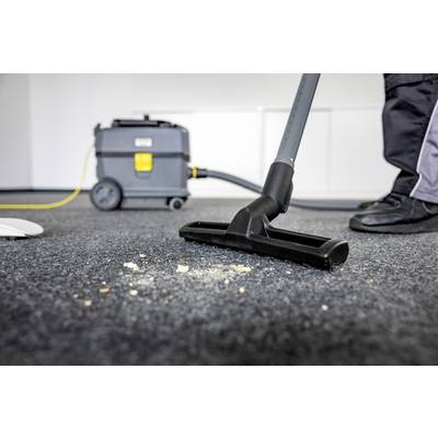 Eine Person saugt Schmutz vom Teppich mit einem Staubsauger. Im Hintergrund ist ein Reinigungsgerät zu sehen.