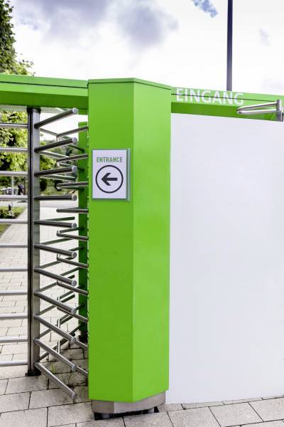 Drehkreuz-Eingang mit Beschilderung 'Eingang' auf Deutsch und 'Entrance' auf Englisch, in einer gehwegseitigen Umgebung.