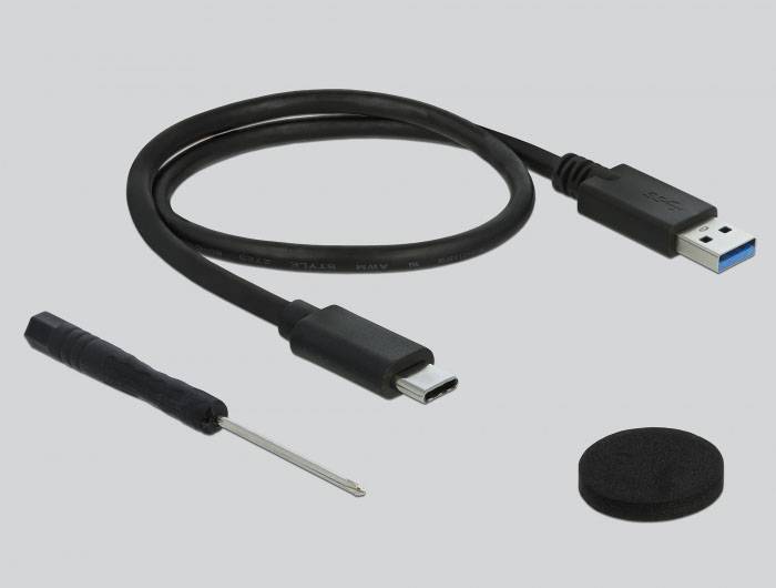 USB-Kabel mit Typ-C-Anschluss, kleiner Schraubendreher und schwarzes, rundes Zubehör auf grauem Hintergrund.