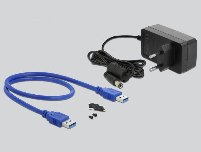 Ein Netzadapter, ein blaues USB-Kabel, drei kleine Schrauben und ein schwarzes Plastikteil liegen auf einer grauen Oberfläche.