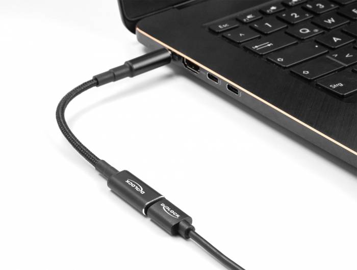 Ein schwarzes Laptop mit einer eingesteckten Ladebuchse, verbunden mit einem geflochtenen Kabel, das an eine Stromquelle angeschlossen ist.