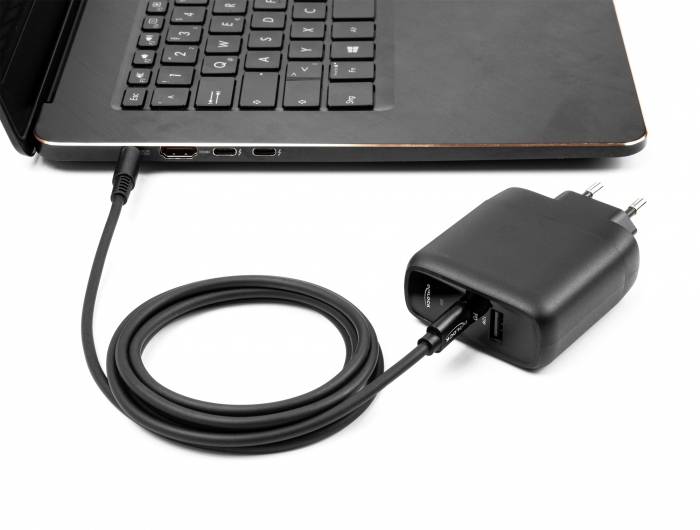 Laptop mit angestecktem Ladekabel, das in ein USB-Ladegerät mit zwei Anschlüssen gesteckt ist. Elektronische Geräte im Ladevorgang.