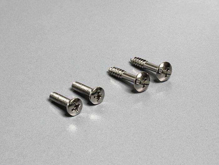 Vier silberne Schrauben unterschiedlicher Größe auf grauem Hintergrund, zwei mit flachem Kopf und zwei mit spitzem Ende.