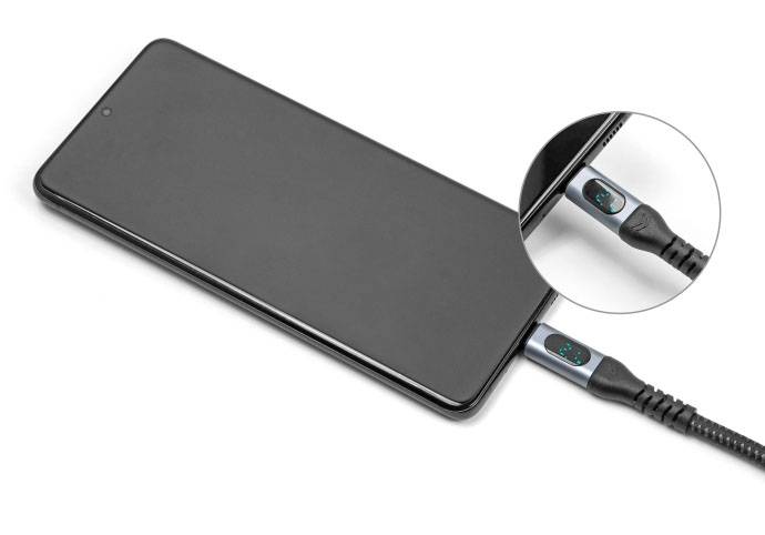 Ein Smartphone wird mit einem USB-Kabel aufgeladen. Ein vergrößerter Kreis zeigt ein Display am Kabelanschluss mit Ladeanzeige.