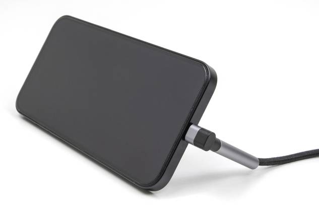 Schwarzes Smartphone liegt quer und wird mit einem Kabel aufgeladen, zeigt keine sichtbaren Inhalte auf dem Bildschirm.