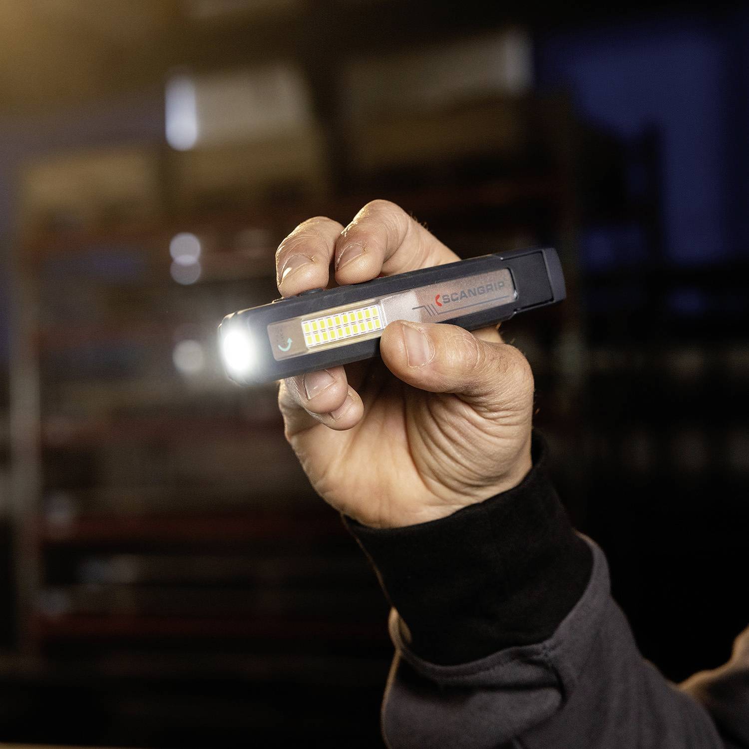 Eine Hand hält eine kompakte LED-Taschenlampe, die einen hellen Lichtstrahl aussendet. Im Hintergrund ist ein unscharfer Raum erkennbar.