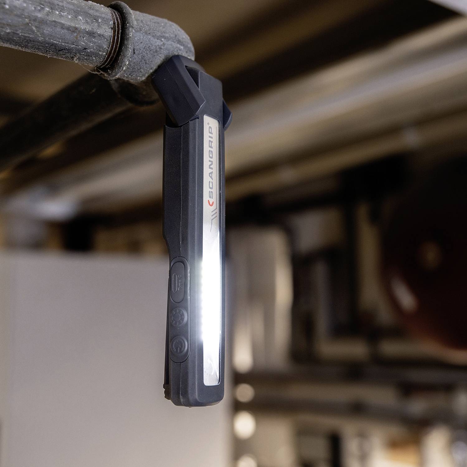 Eine tragbare LED-Taschenlampe leuchtet auf eine Metallleitung in einem industriellen Umfeld. Die Taschenlampe ist an der Leitung befestigt.