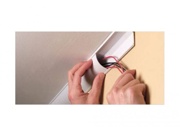 Eine Person installiert Kabel in einem Kabelkanal an der Wand. Sichtbare Kabel sind rot und schwarz.