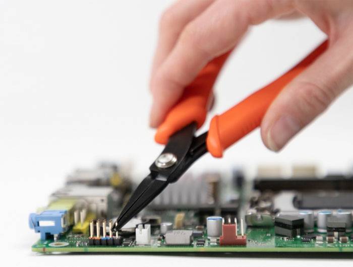 Eine Hand hält eine Zange und bearbeitet eine Computerplatine, wahrscheinlich bei der Reparatur oder Montage von Elektronikkomponenten.