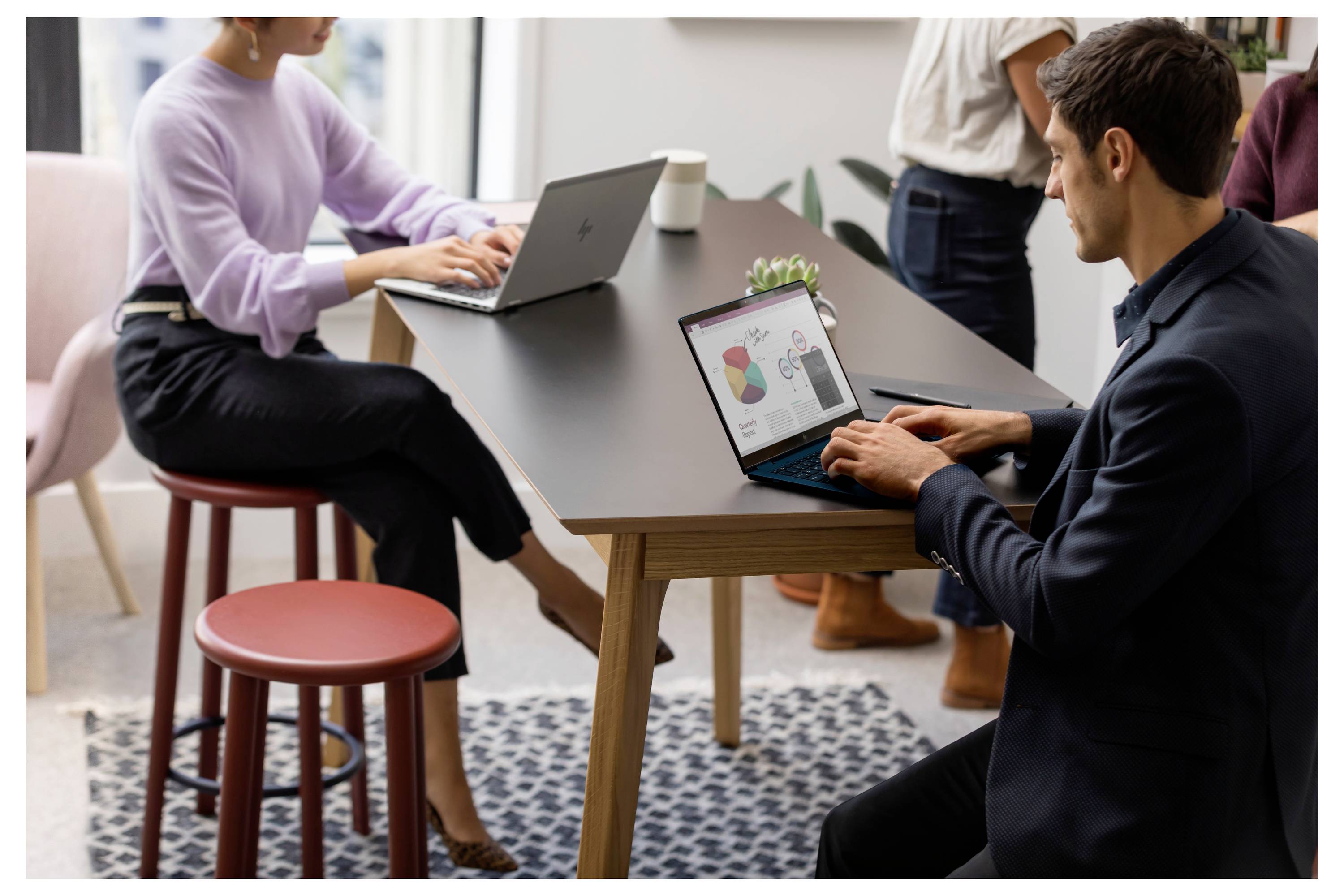 Zwei Personen arbeiten an Laptops an einem Tisch in einem modernen Büro. Eine Person betrachtet ein Daten-Diagramm auf dem Bildschirm.