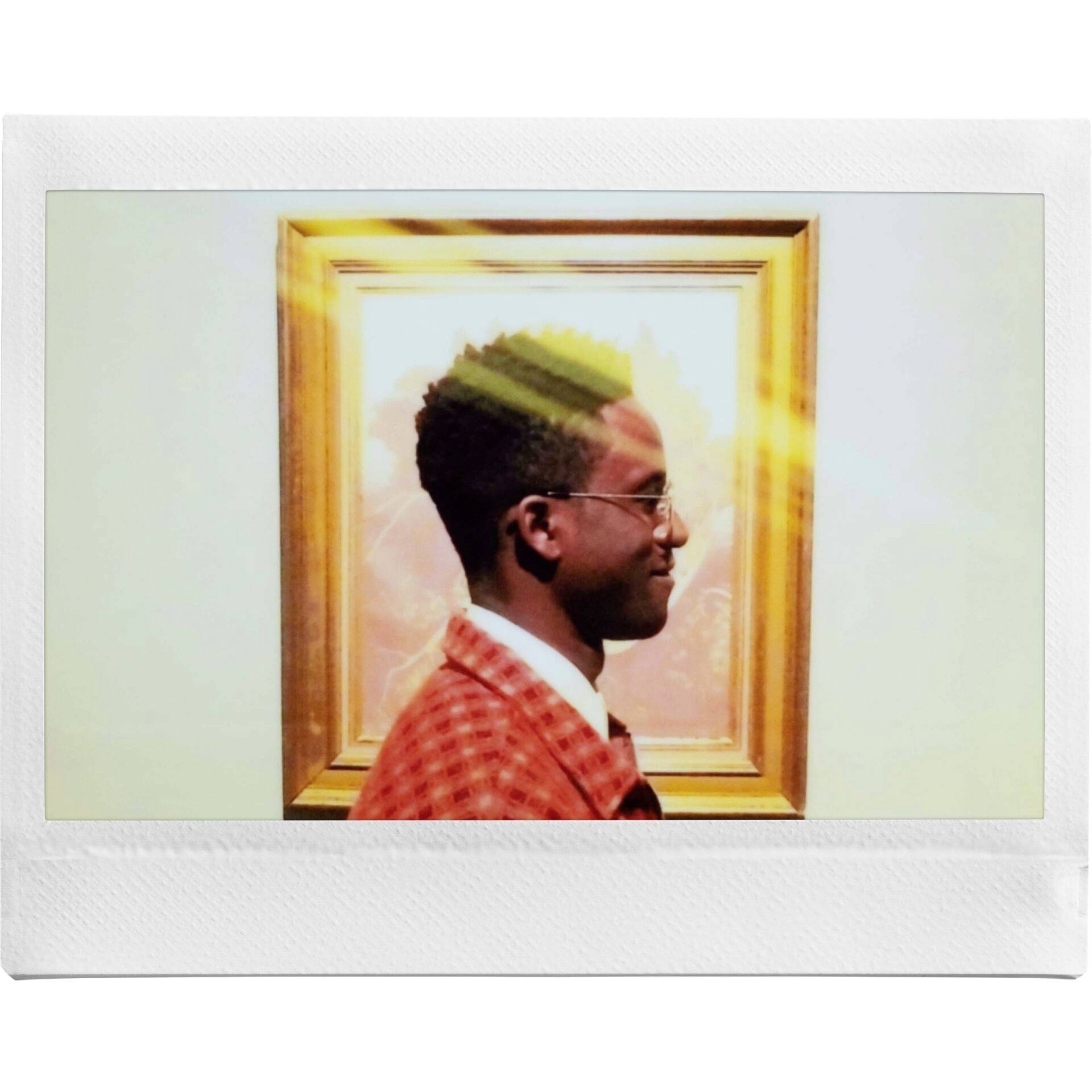 Eine Person steht seitlich vor einem gerahmten Kunstwerk. Sonnenstrahlen scheinen auf das Bild. Die Person trägt eine karierte Jacke.