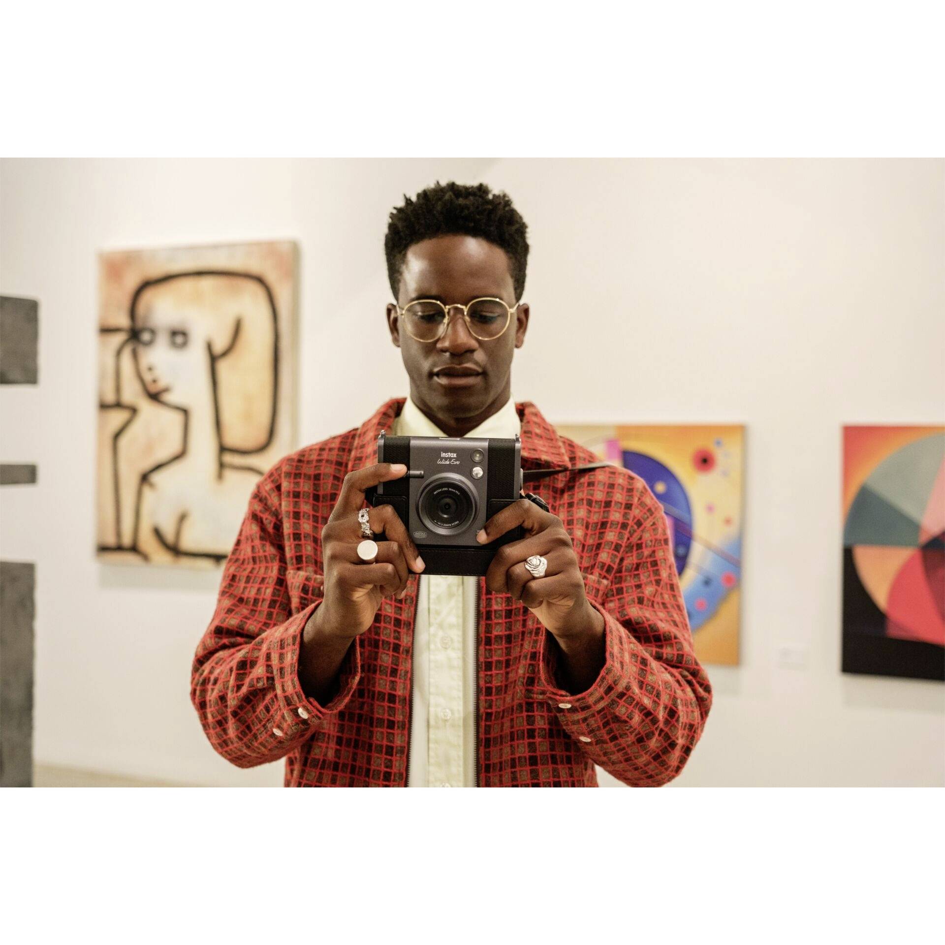 Eine Person steht in einer Kunstgalerie, hält eine Kamera und ist von modernen Gemälden umgeben. Die Atmosphäre ist kreativ und nachdenklich.