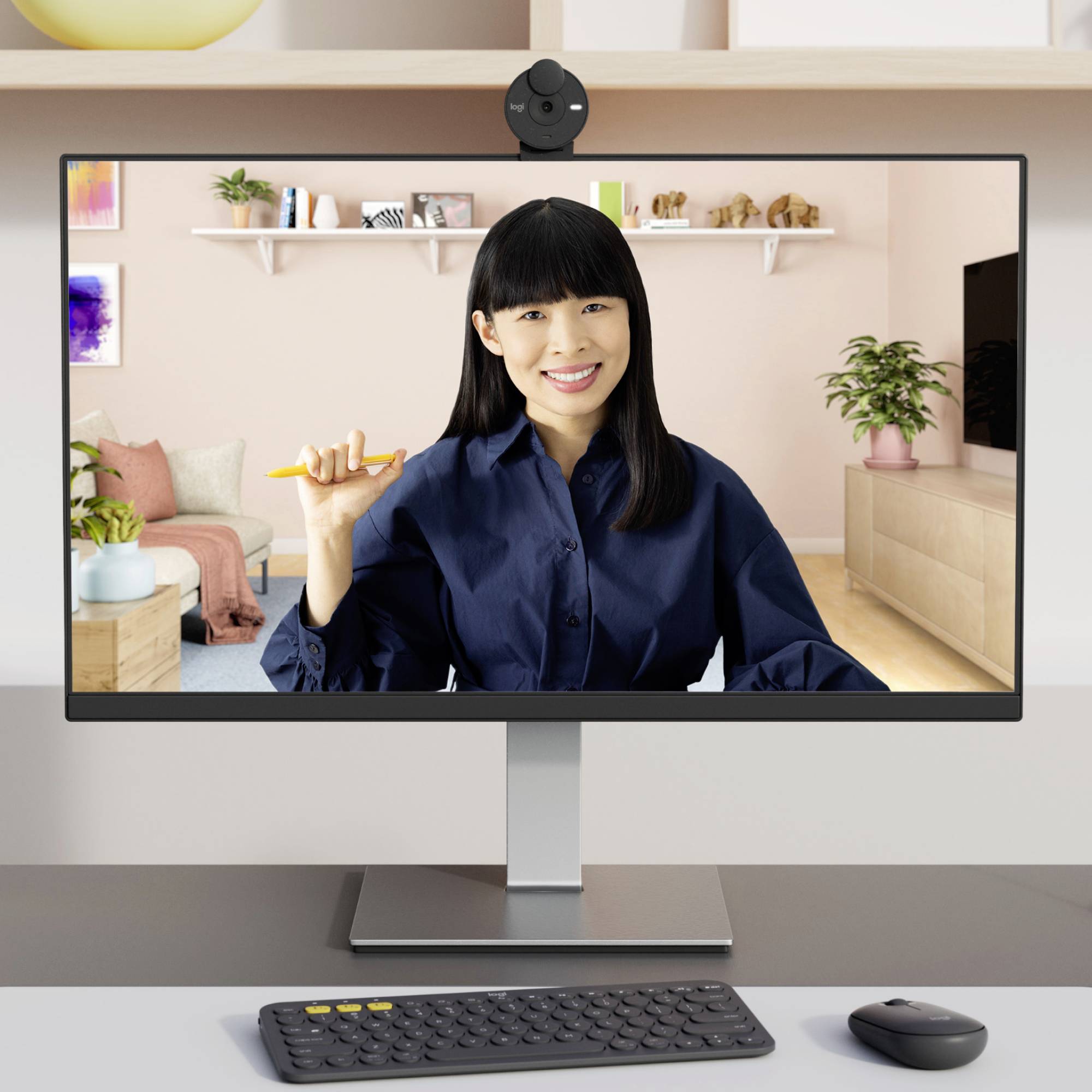 Eine lächelnde Person hält einen Stift in der Hand und sitzt vor einem Monitor. Im Hintergrund ist ein gemütlich eingerichtetes Zimmer.