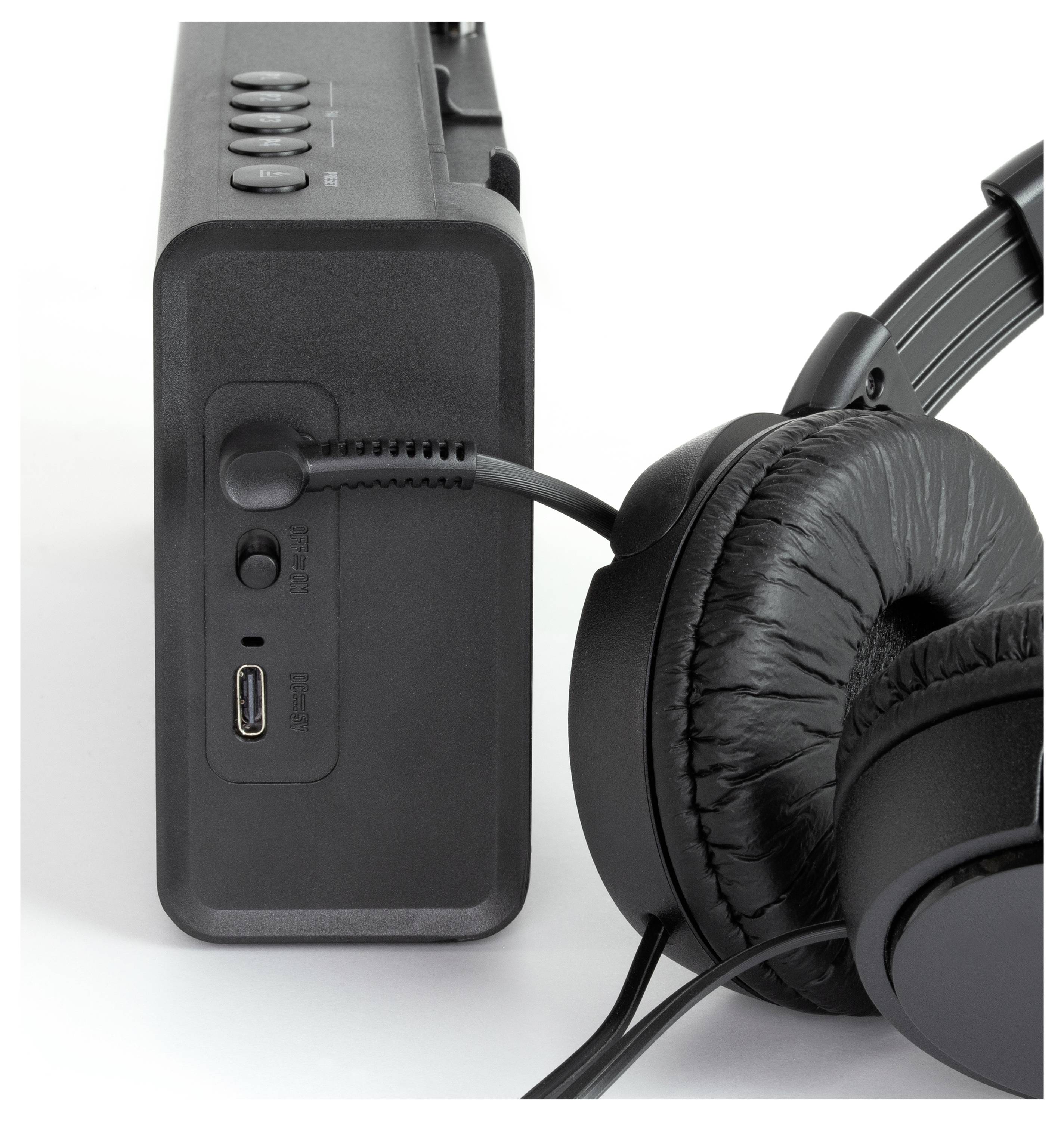 Ein schwarzer Kopfhörer ist mit einem tragbaren Lautsprecher verbunden. Der Lautsprecher zeigt Knöpfe und Anschlüsse an der Seite.